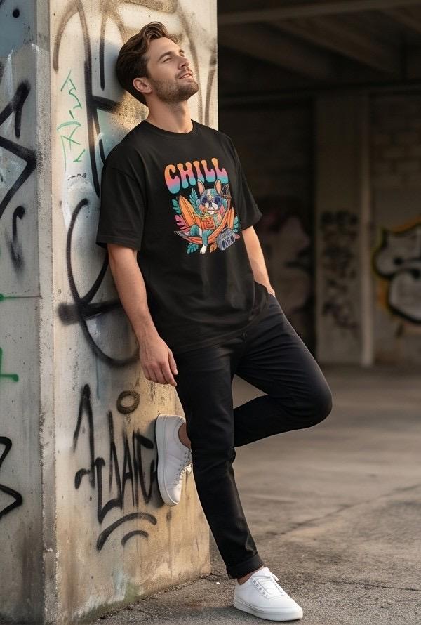 Man in black graphic t-shirt and black pants leaning on wall